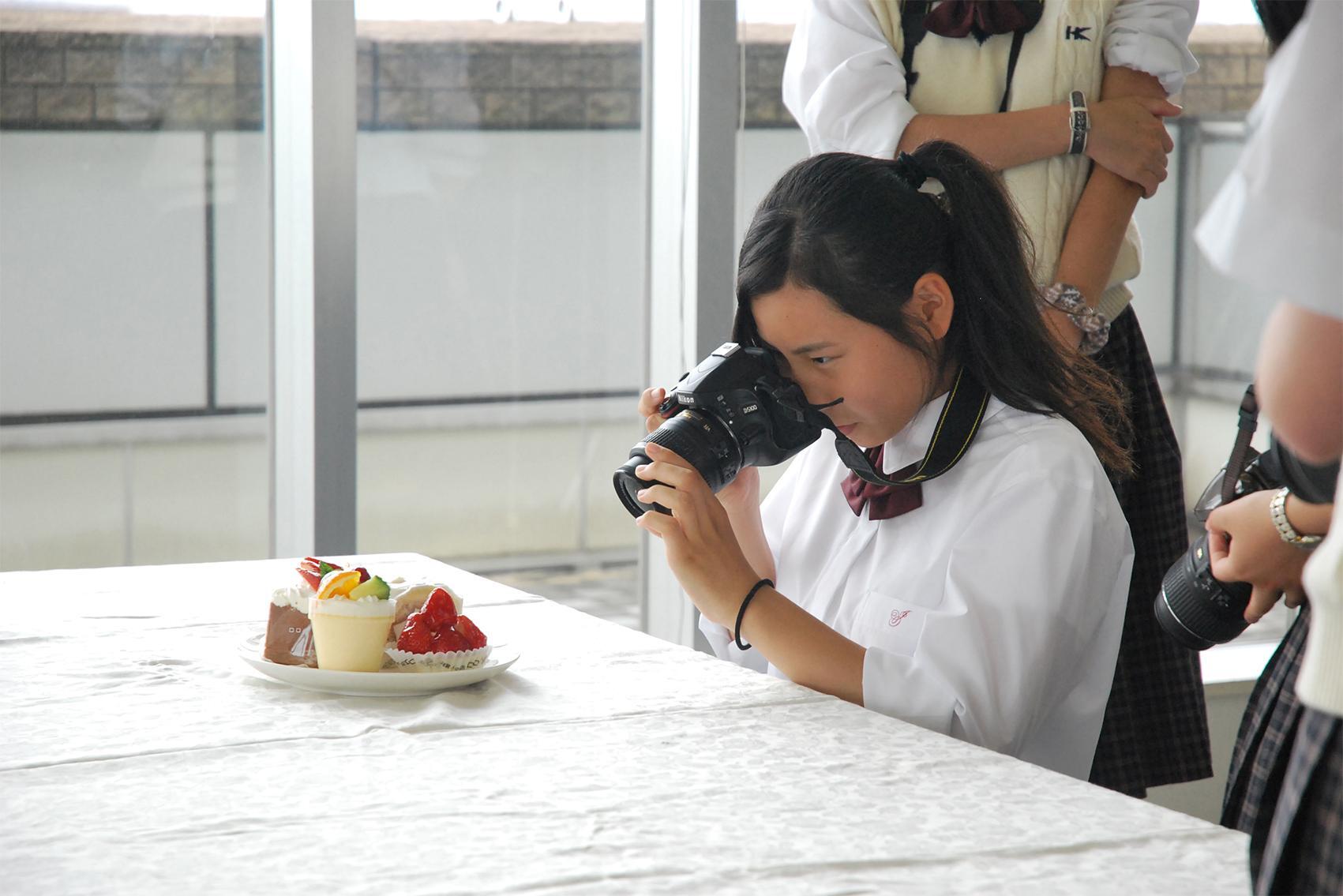 女生徒が皿に乗ったケーキを撮影している写真